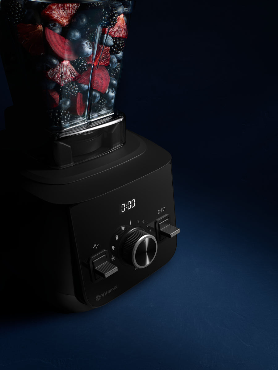A black Vitamix blender filled with mixed berries and fruit, shown at an angle on a dark blue background.