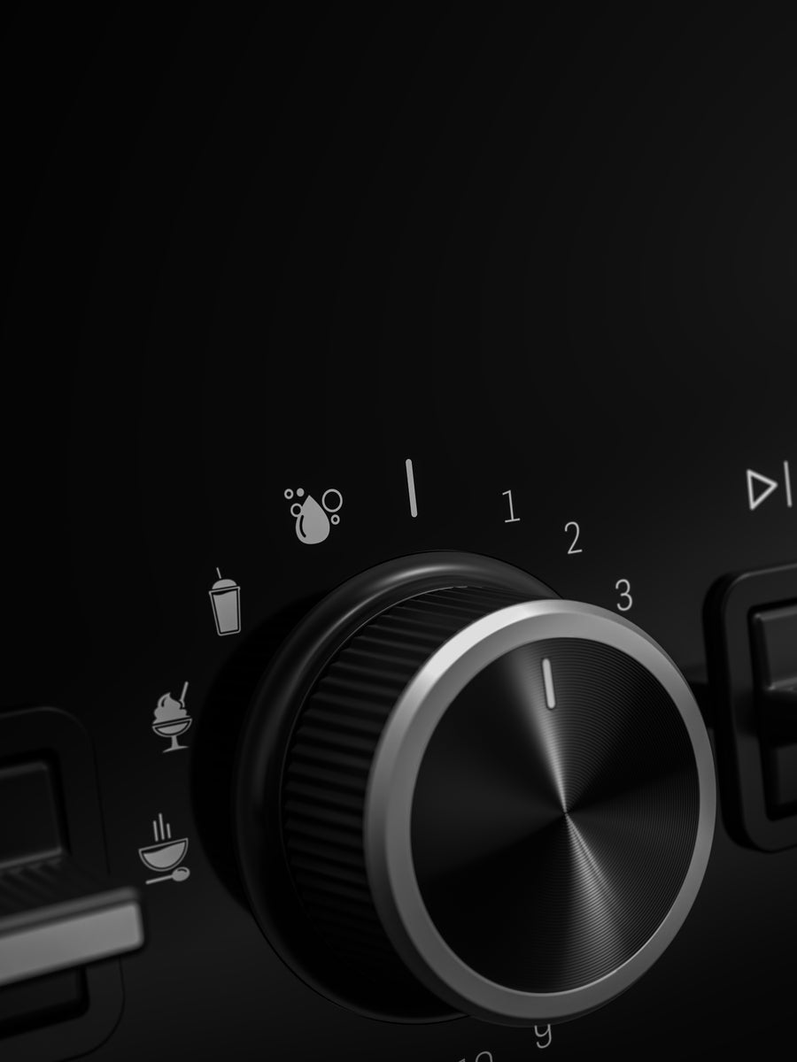 Close-up of a Vitamix X2 black rotary control knob with silver metallic trim and white printed icons and numbers on a dark surface.