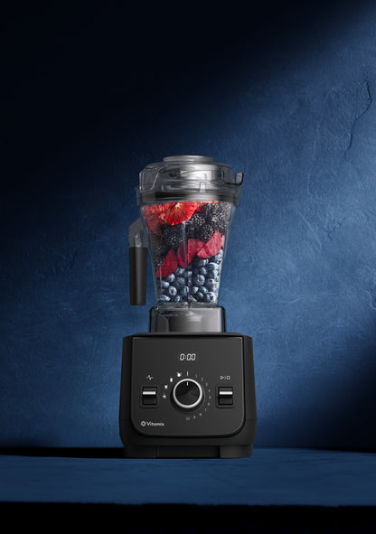 A black Vitamix blender with a clear container filled with blackberrie and blue blueberries, set against a dark textured blue background.