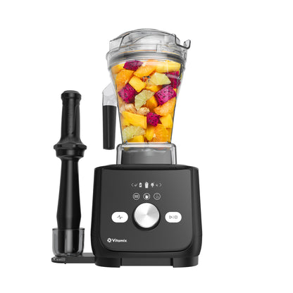 A Vitamix Ascent X5 blender with a black base and a clear blender jug filled with colourful fruit pieces, shown alongside a black tamper on a plain white background.