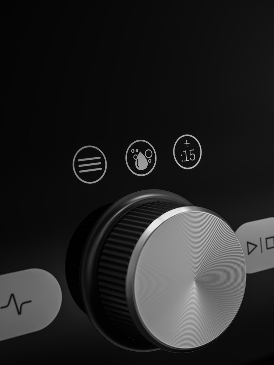 Close-up of a black Vitamix Ascent X5 control panel with a large silver rotary knob and three small white icons above it, including a menu icon, a droplet icon, and a plus sign with '+15'.