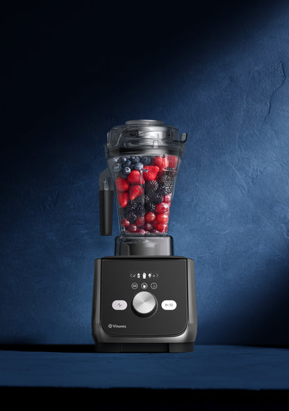 A Vitamix Ascent 5X blender with a clear container filled with mixed berries, set against a dark blue textured studio background.