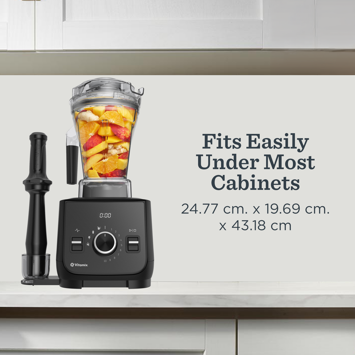 A Vitamix Ascent X blender with a clear jar filled with fruit sits on a white kitchen countertop, alongside a black tamper and a small clear container. Text on the right reads 'Fits Easily Under Most Cabinets' with dimensions.